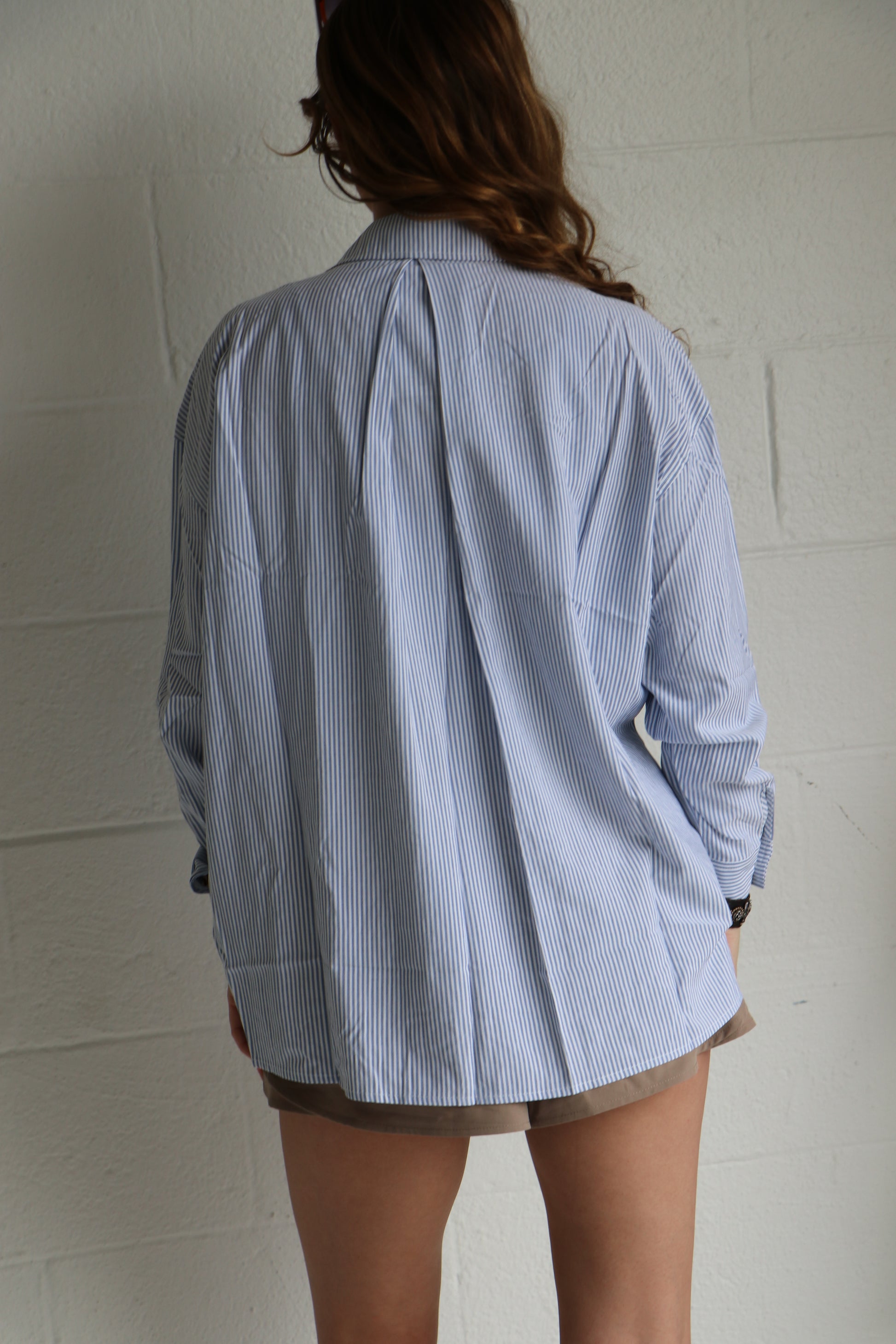 Person wearing a light blue striped shirt and beige shorts on a white background