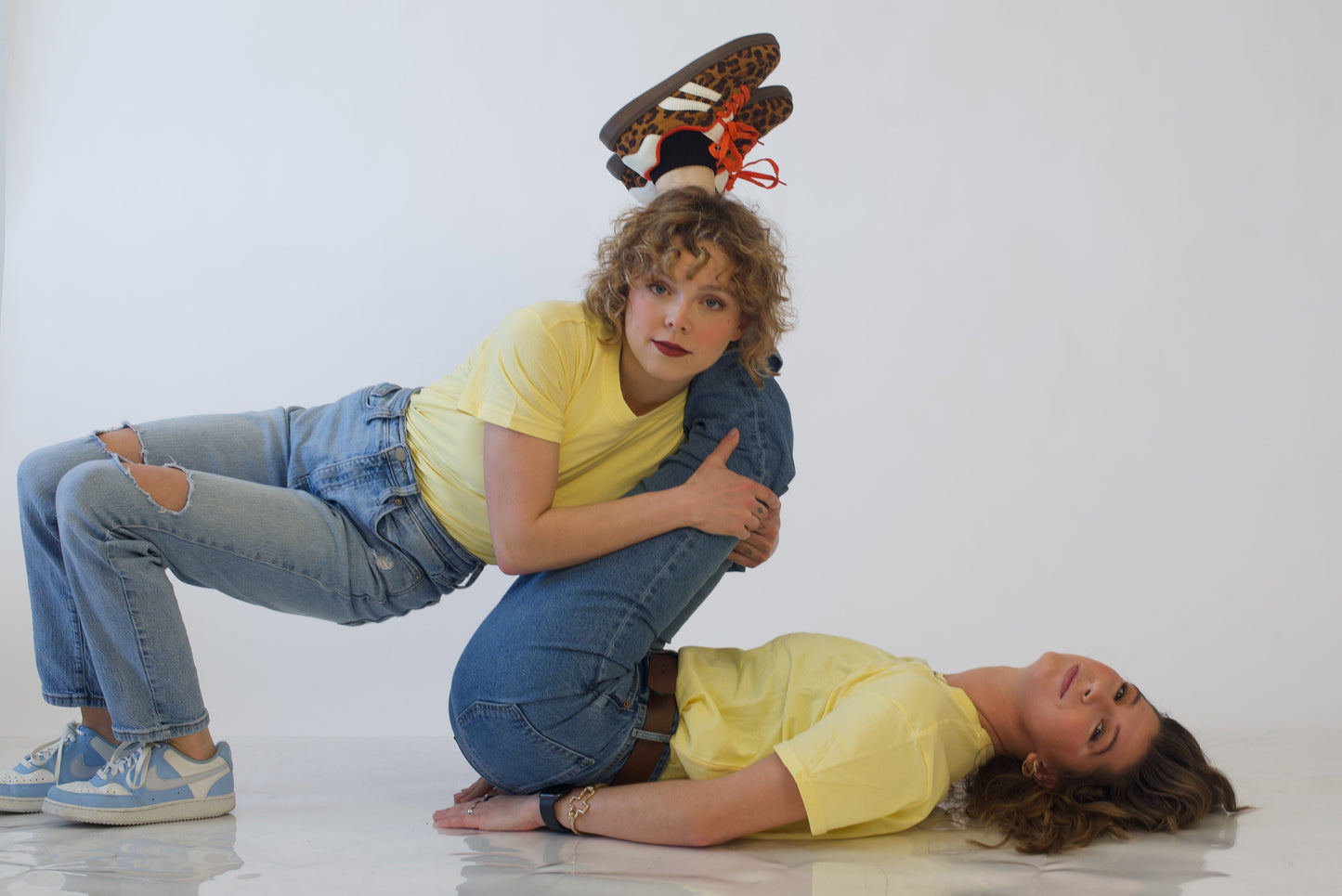 Two people in yellow shirts and jeans doing a funny pose on a white background