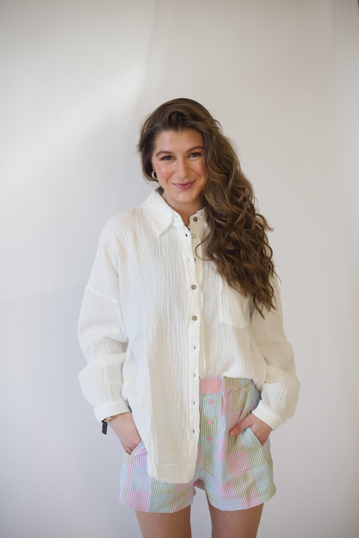 Woman wearing a white button-up shirt and colorful shorts against a plain background