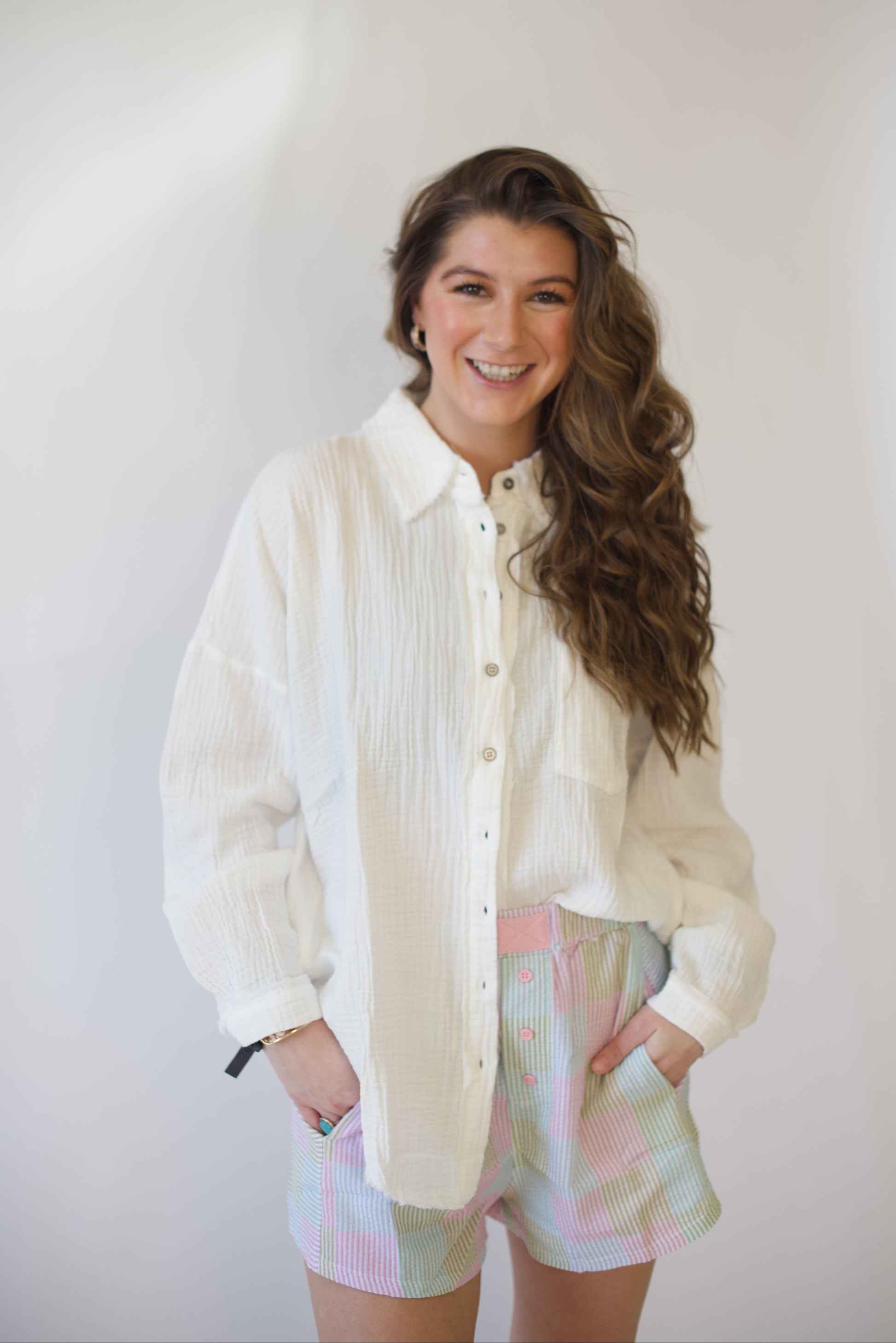 Woman wearing a light-colored shirt and pastel shorts against a plain background