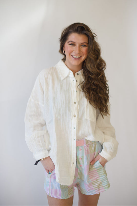 Woman wearing a light-colored shirt and pastel shorts against a plain background