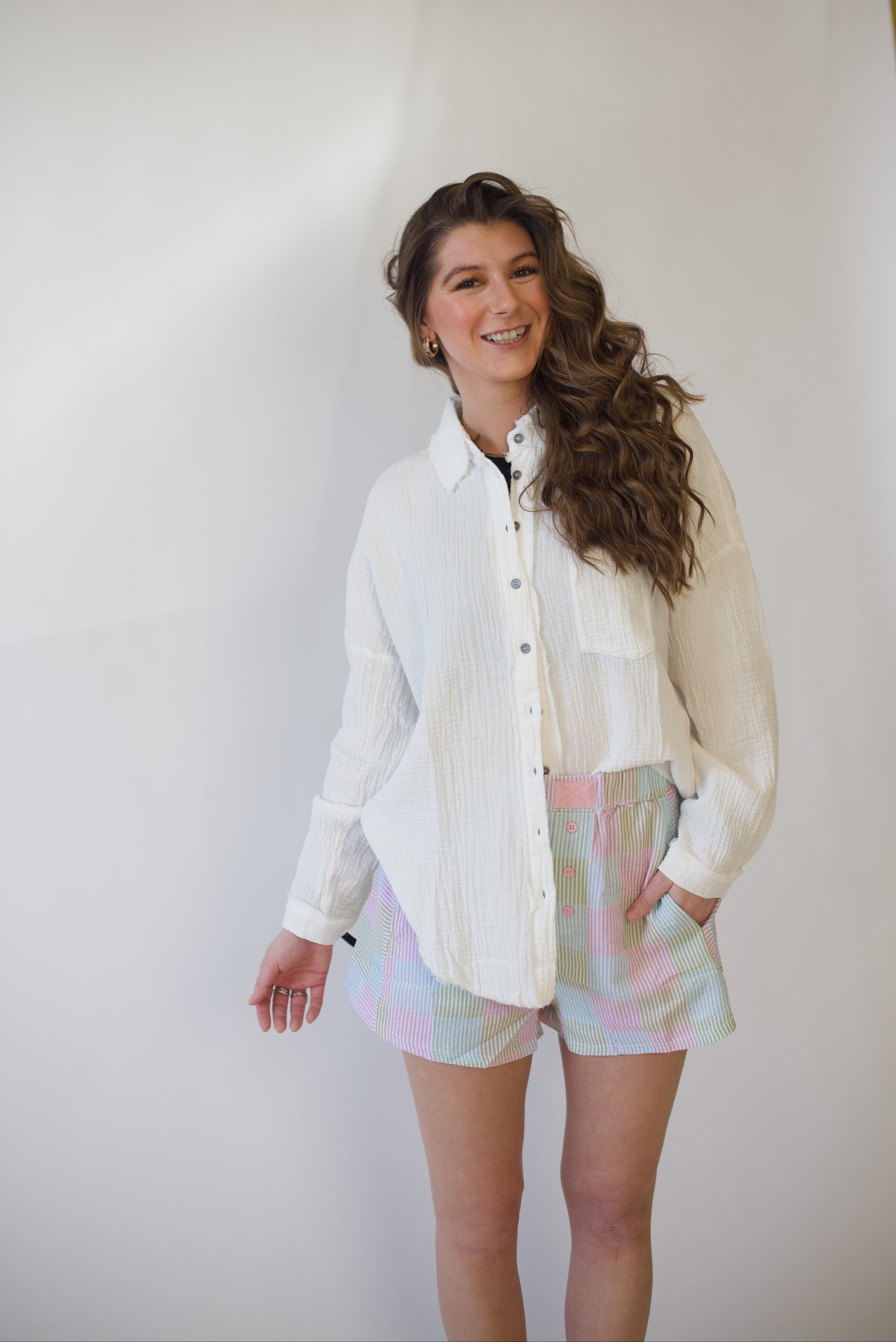 Woman wearing a white button-up shirt and pastel shorts against a plain background