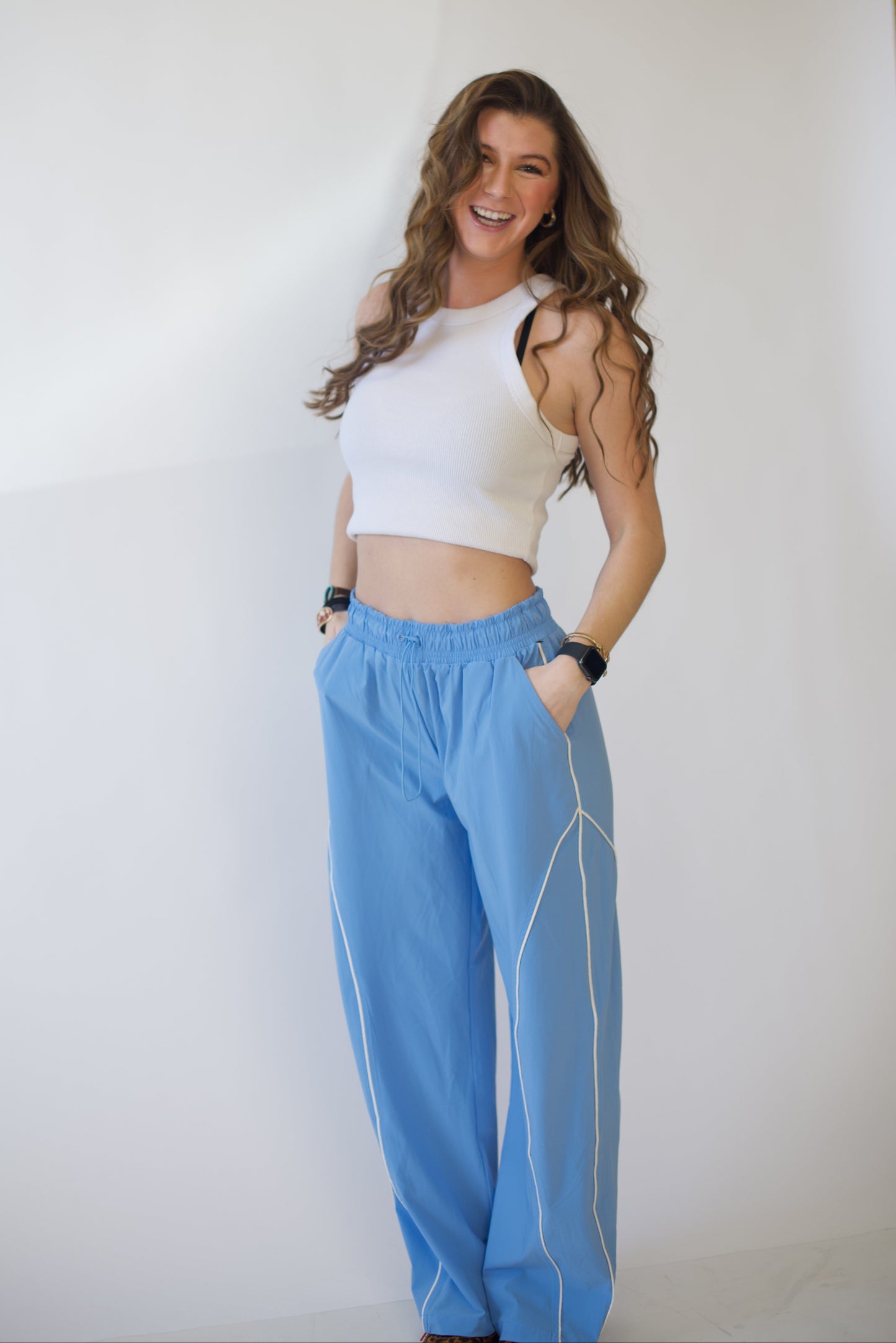 Woman wearing a white top and blue track pants against a plain background