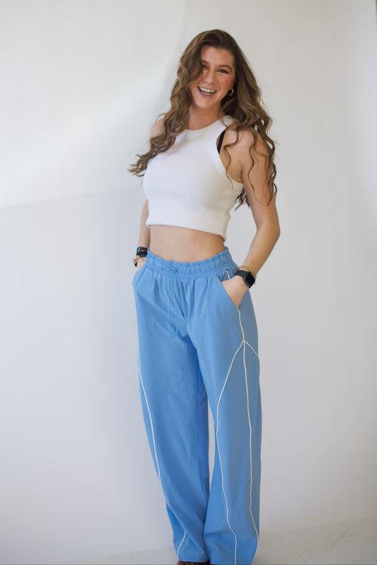 Woman wearing a white top and blue track pants against a plain background