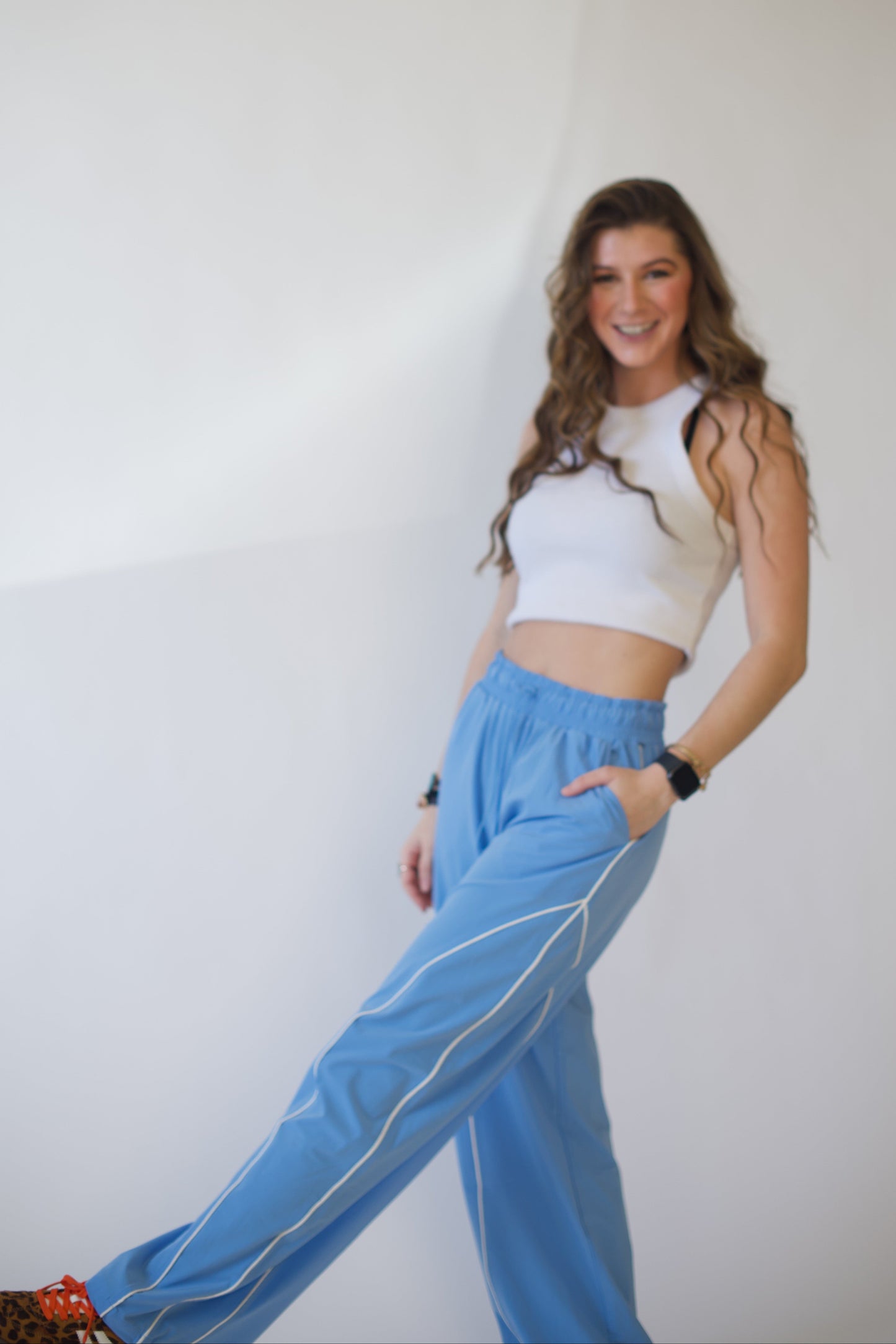 Woman wearing a white top and blue track pants against a plain background