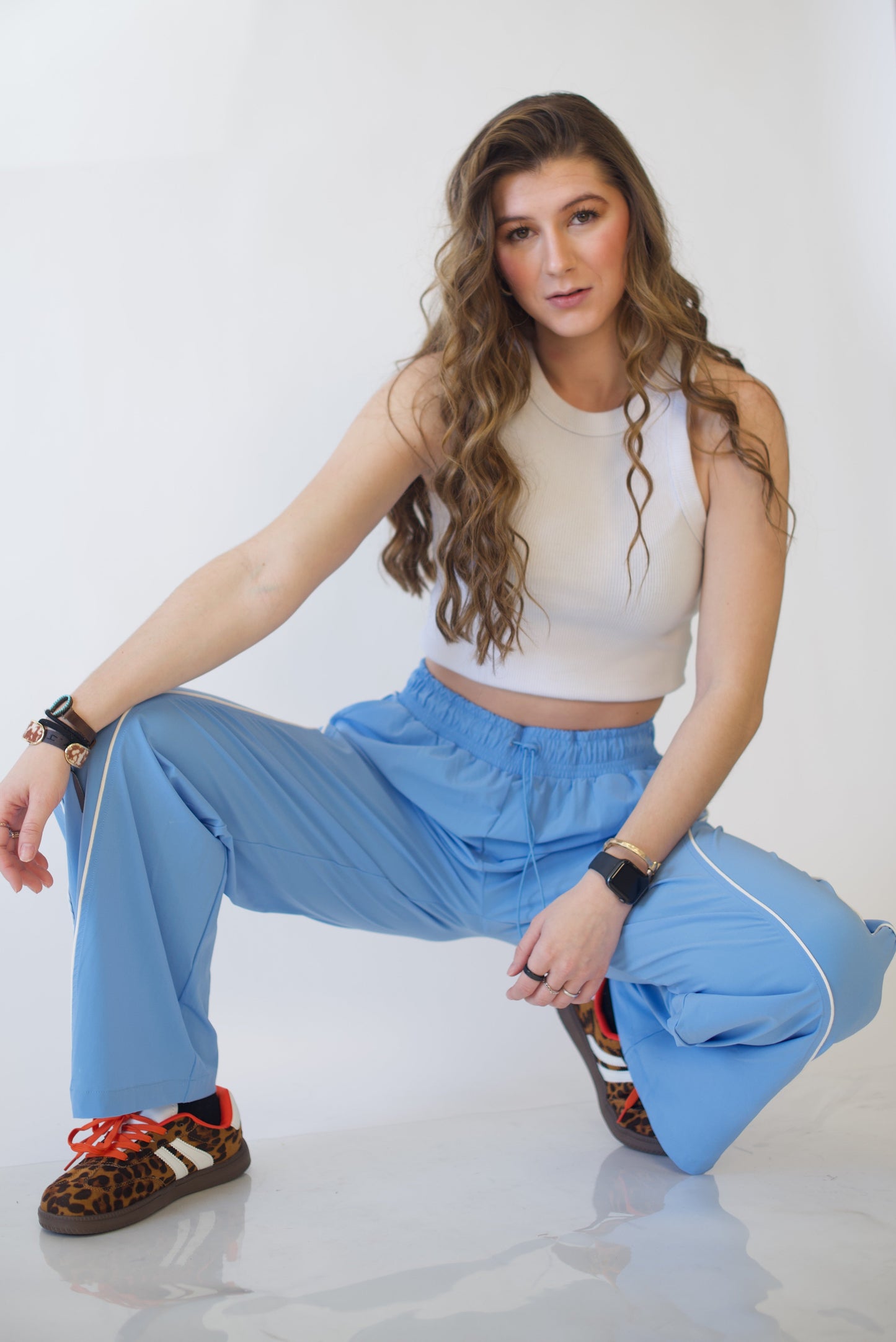Woman in a white top and blue track pants sitting on the floor against a white background
