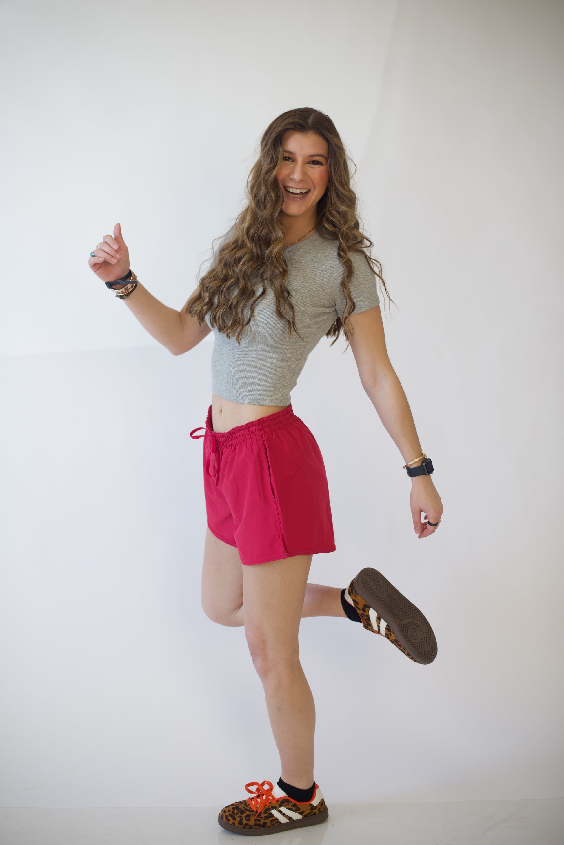 Woman in a gray crop top and pink shorts spinning against a white background