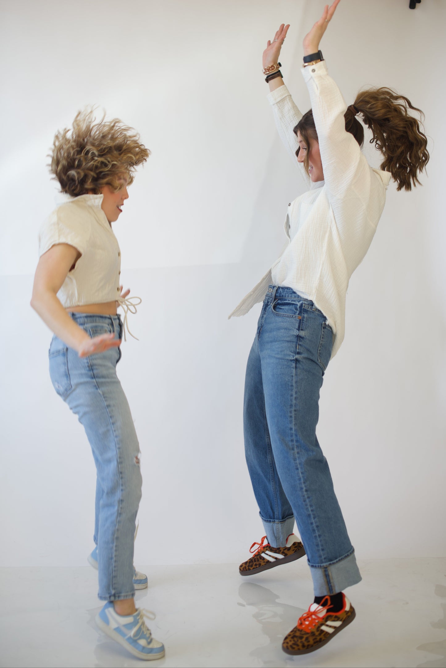 Two people in jeans and white button up shirts jumping on a white background