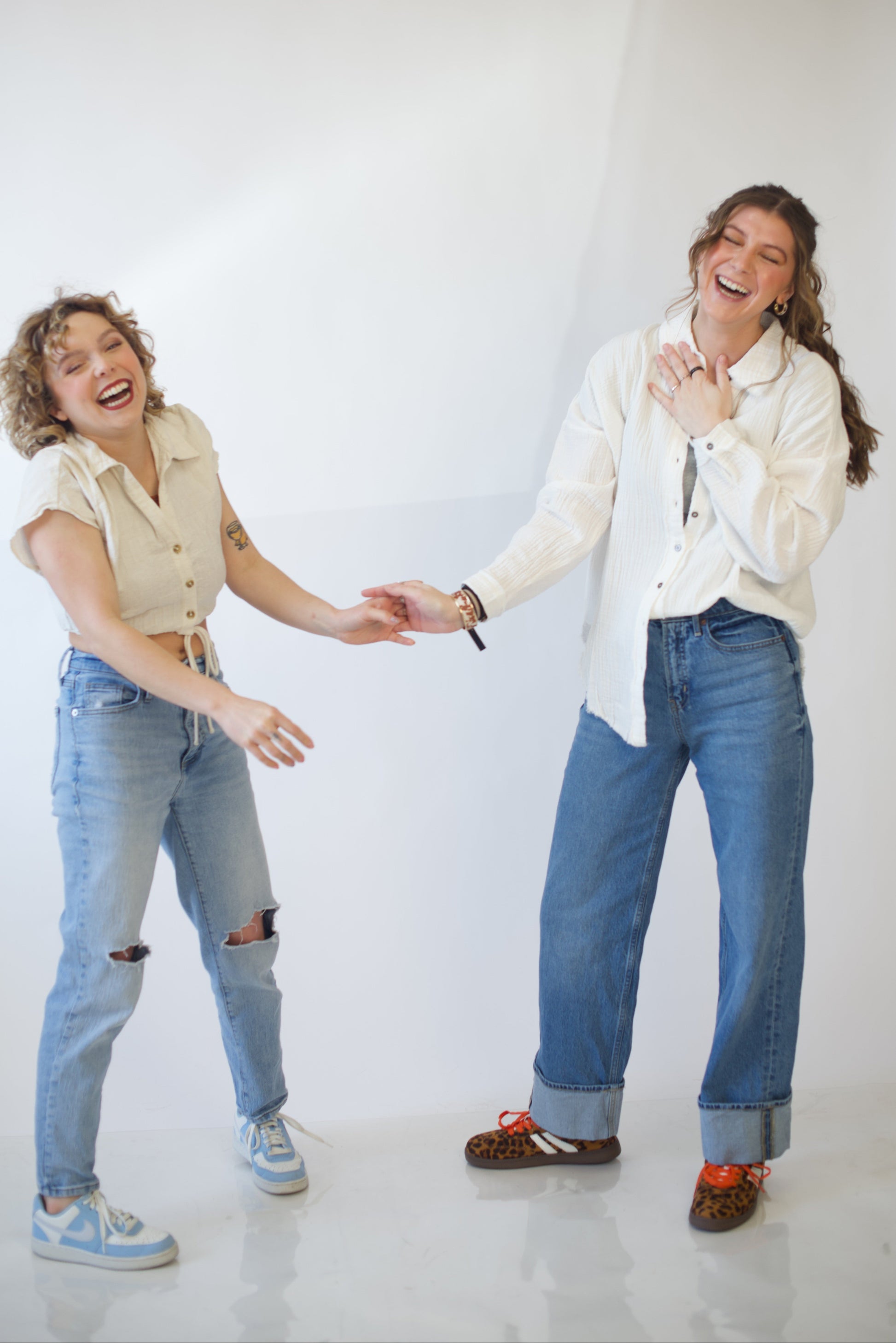 Two people laughing and holding hands against a white background