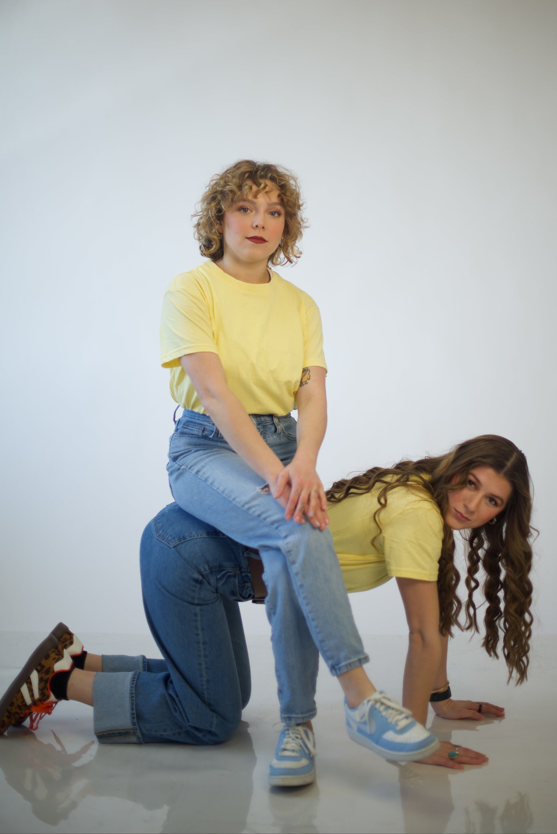 Two people wearing yellow shirts and blue jeans posing against a white background.