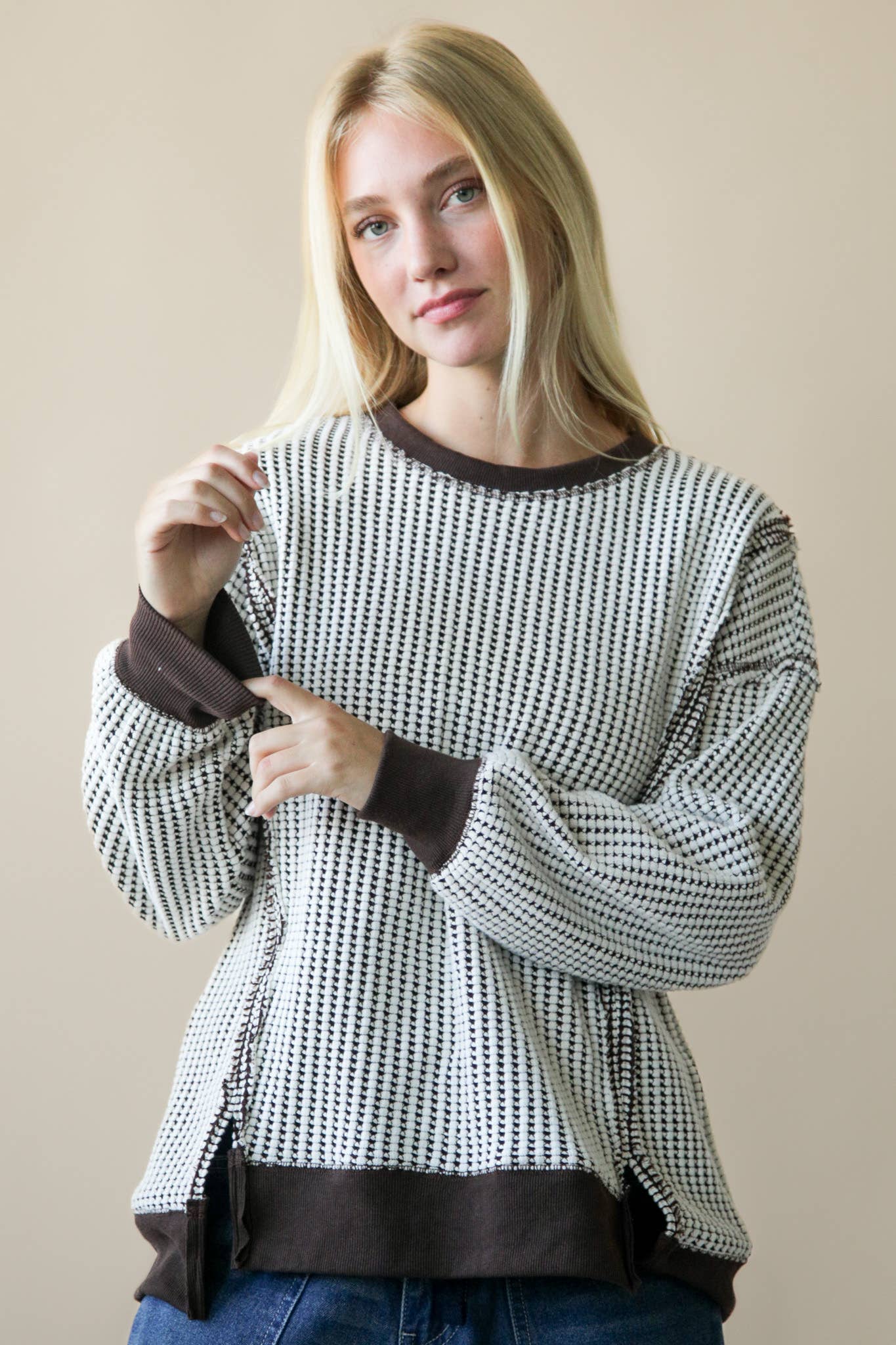 Woman wearing a black and white patterned sweater with brown trim against a beige background